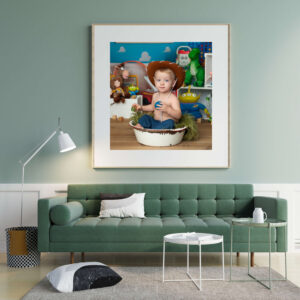 A living room with a green sofa and white tables, featuring a large framed photo by a cake smash photographer Jacksonville FL, showing a young child in a cowboy hat sitting in a bowl, surrounded by Toy Story-themed toys above the sofa.