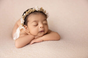 A newborn baby with a floral headband sleeps peacefully on a soft, light-colored blanket, arms tucked under the chin and eyes closed—captured beautifully by a Jacksonville baby photographer.