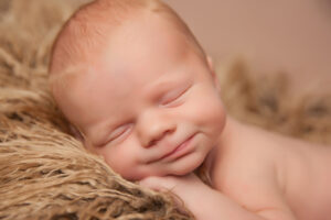 A newborn baby with closed eyes and a gentle smile sleeps peacefully on a soft, fluffy brown blanket, resting its head on its hands—a heartwarming moment captured by Jacksonville newborn photography.